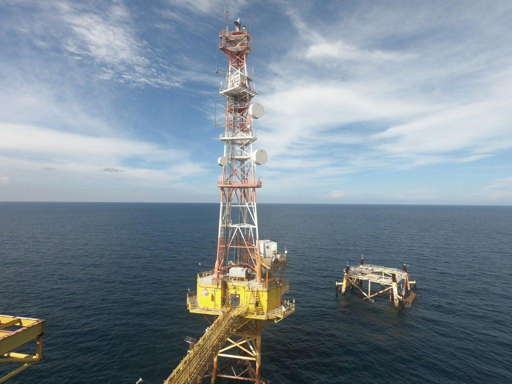 Offshore platform with tall communication tower on blue ocean.